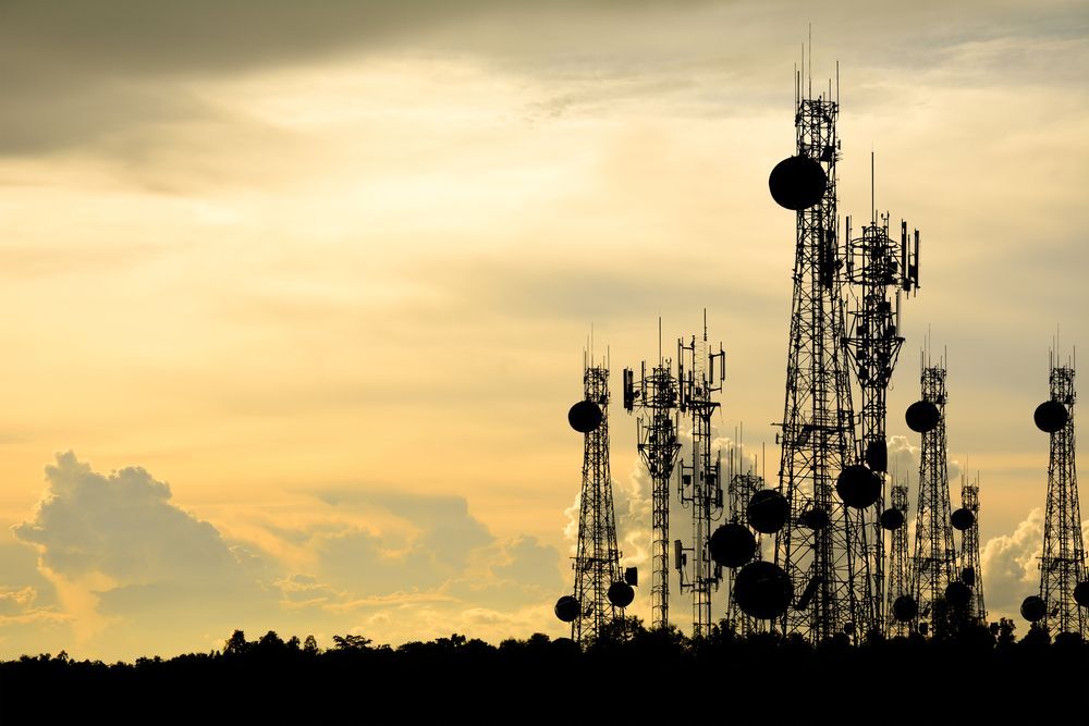 A bunch of antennas are silhouetted against a cloudy sky.