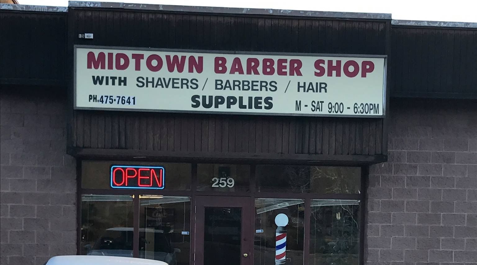 A white car is parked in front of a midtown barber shop