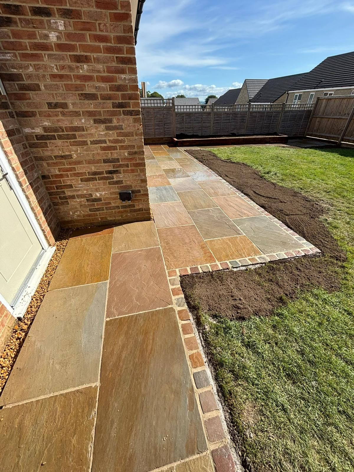 Brick house patio with multicolored stone walkway and grass lawn beside a fenced backyard.