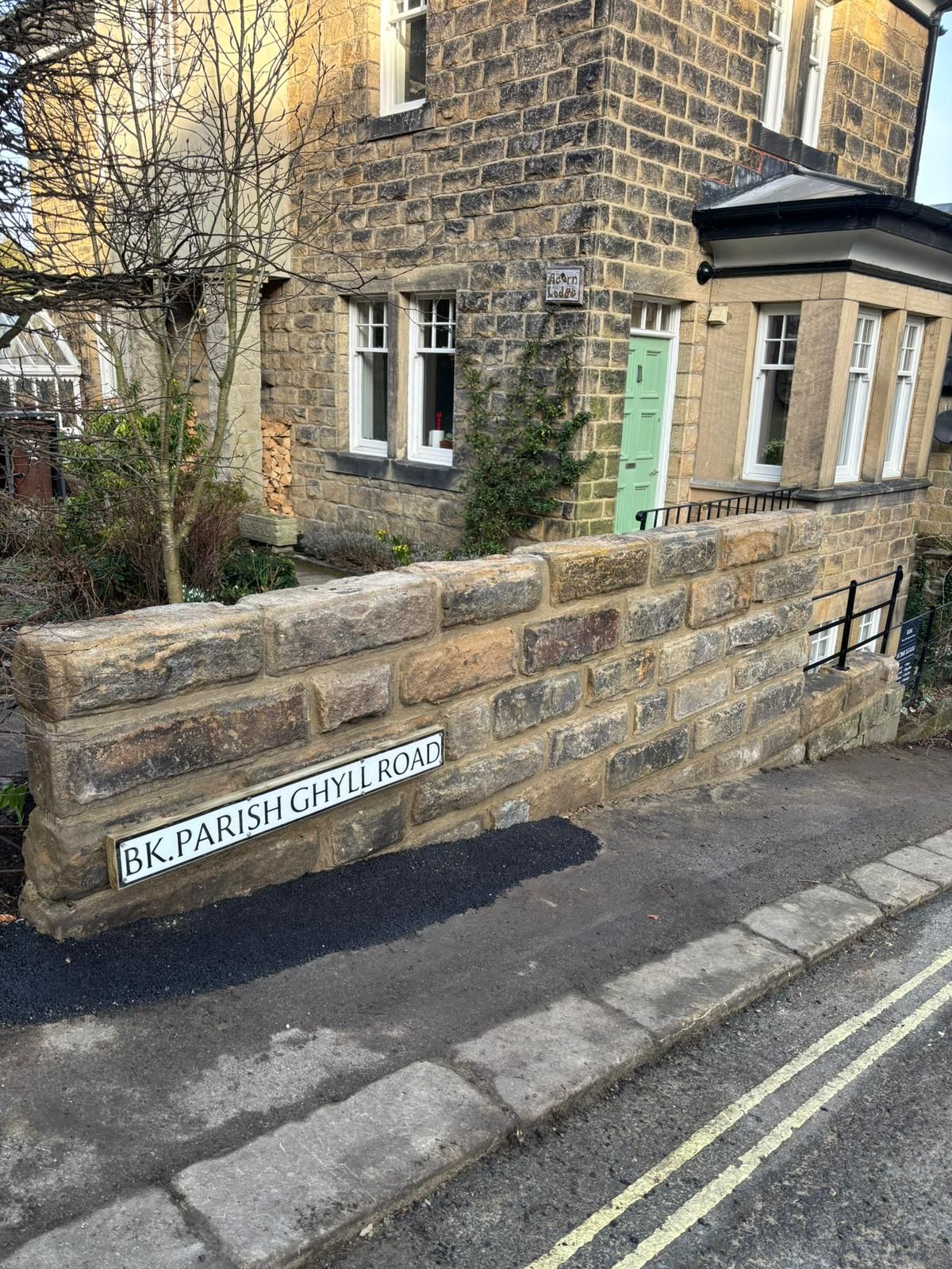 Stone house corner with green door and low wall on a quiet street with double yellow lines