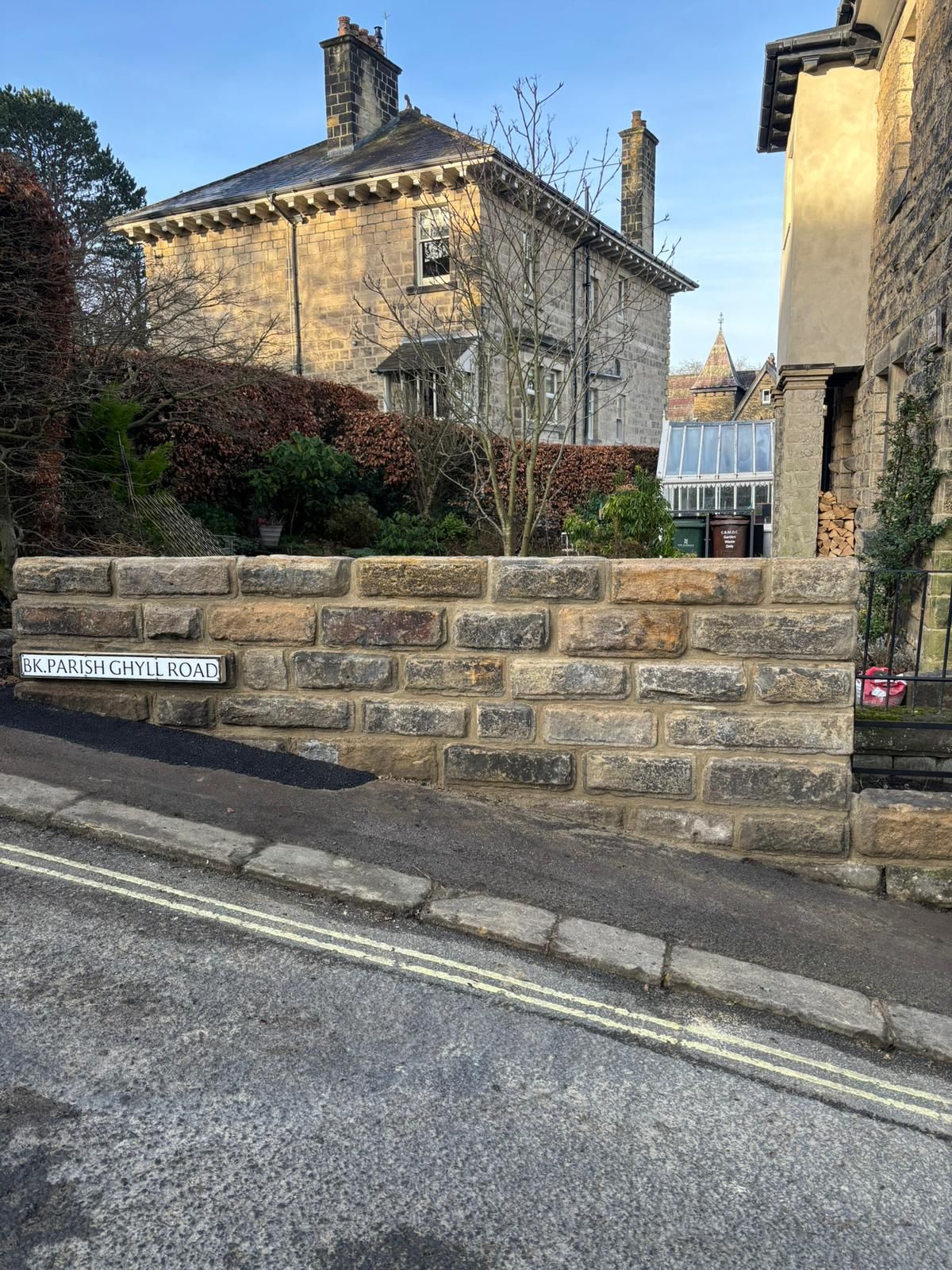Stone house behind a low stone wall on a narrow street, with an alley opening beside it.