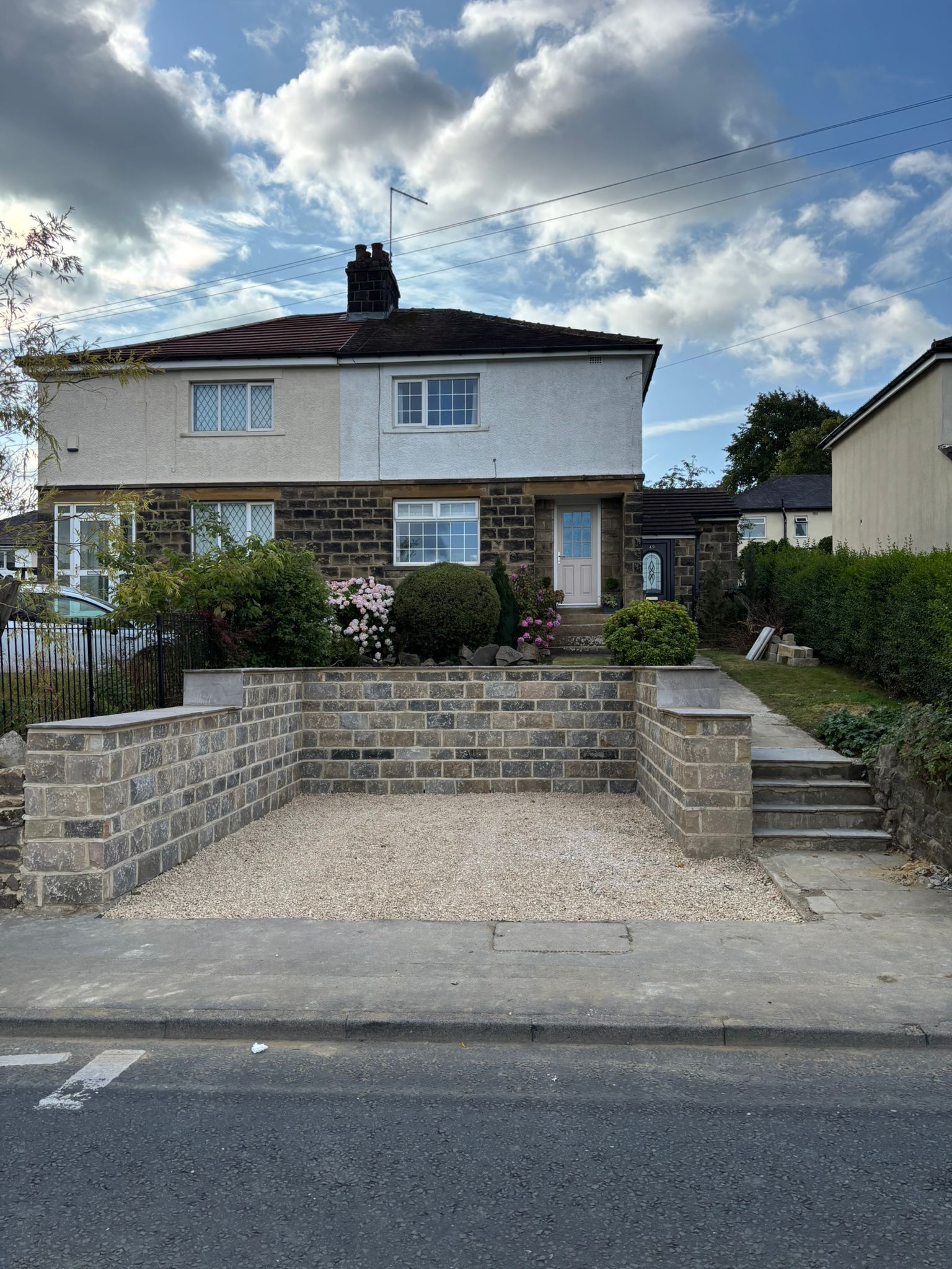 Semi-detached house with stone front garden wall, gravel driveway, and cloudy sky