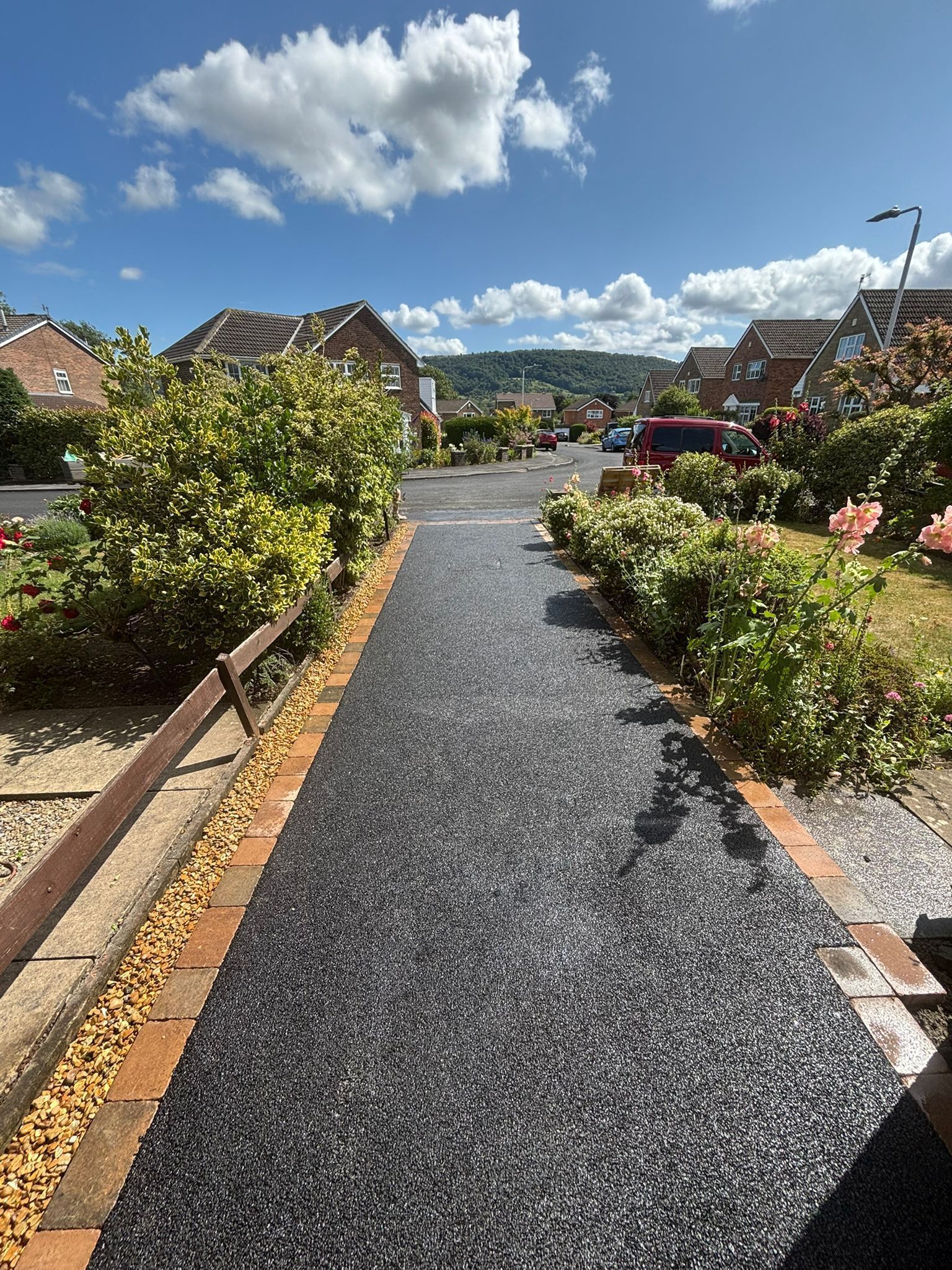 Gravel path through landscaped garden under a bright blue sky with houses in the distance