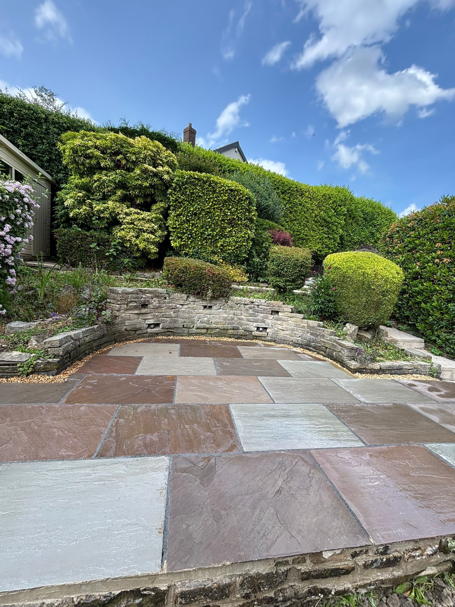Stone patio leading to a lush green hillside garden under a bright blue sky