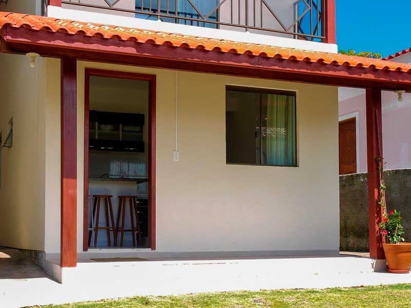 Edifício bege claro com telhado de telhas vermelhas e porta aberta; interior da cozinha visível.