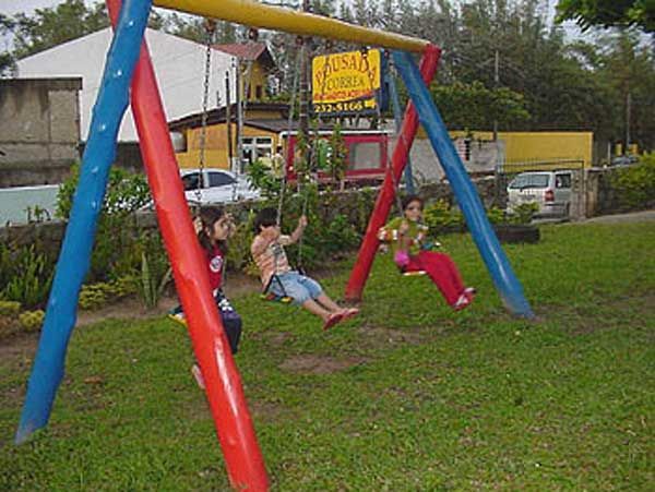 Crianças se balançando em um balanço colorido em um parque gramado.
