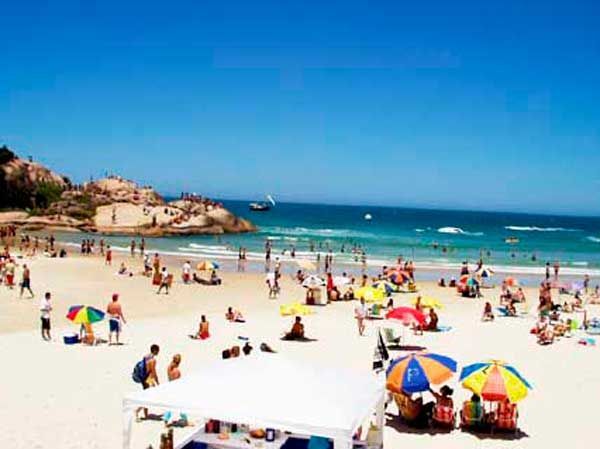 Igreja branca e laranja com porta em arco, degraus e uma cruz no topo, sob um céu azul.