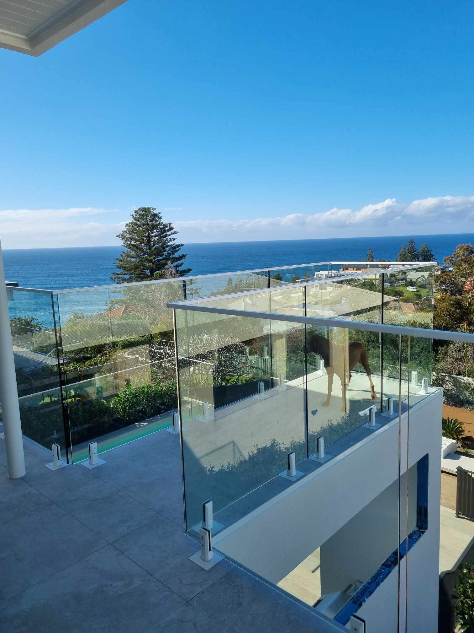 A Balcony With a Glass Railing Overlooking the Ocean — D & T Balustrade Systems In Unanderra, NSW