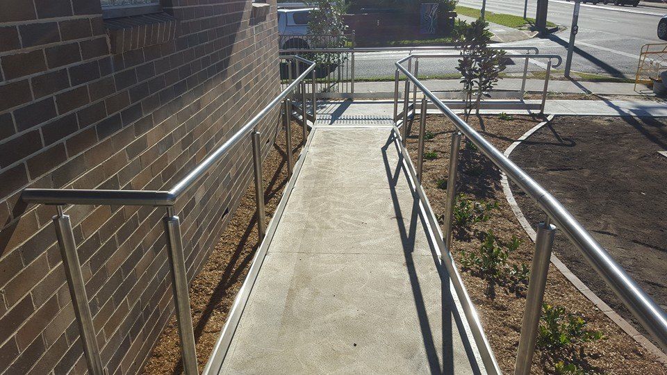 A concrete ramp with metal railings alongside a brick building — D & T Balustrade Systems In Unanderra, NSW