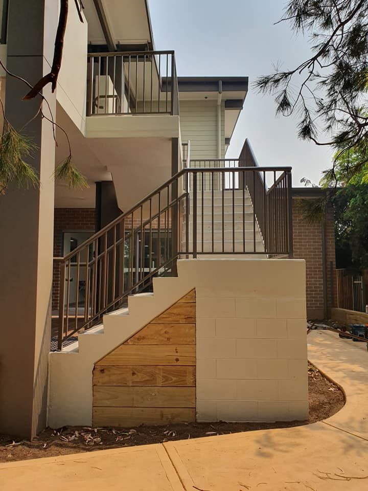 Exterior stairs with metal railings leading to a building. Off-white walls, wooden accents — D & T Balustrade Systems In Unanderra, NSW