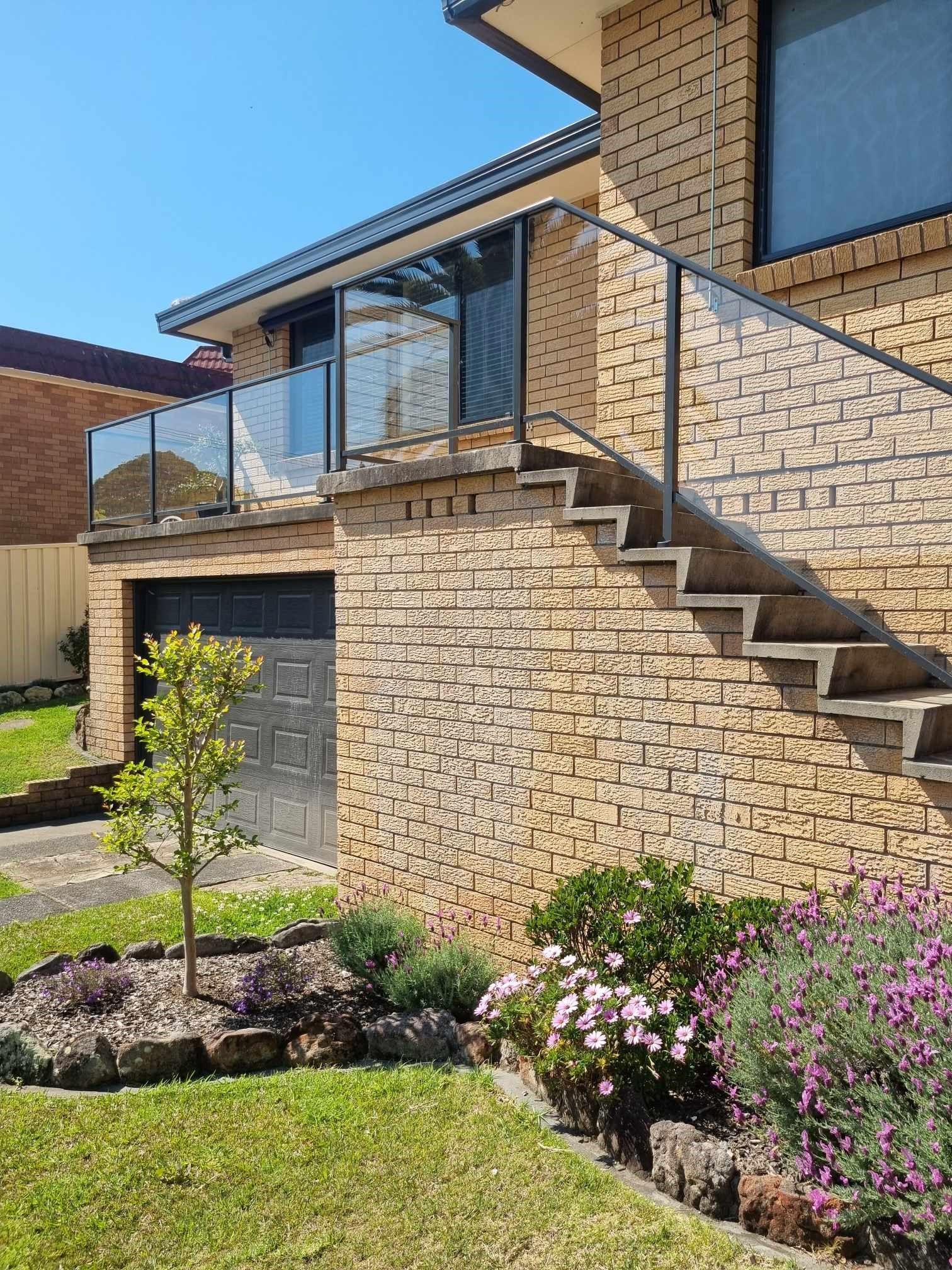 A Man is Standing in Front of a House With Stairs Leading Up to It — D & T Balustrade Systems In Unanderra, NSW
