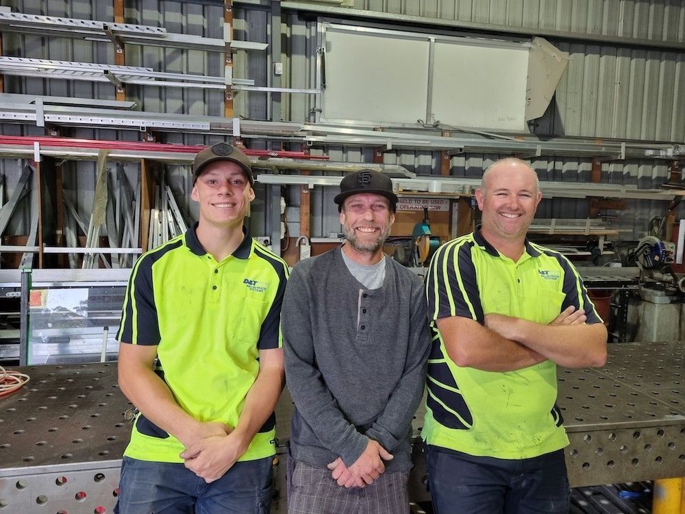 Three Men Are Posing for a Picture in a Garage — D & T Balustrade Systems In Unanderra, NSW