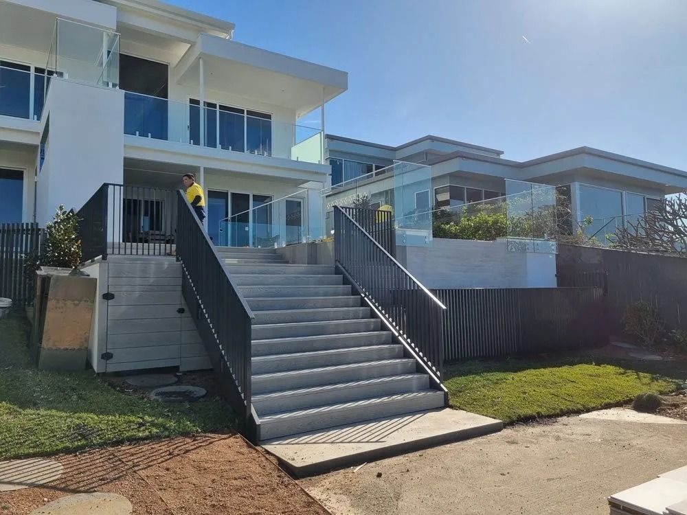 A Man is Standing in Front of a House With Stairs Leading Up to It — D & T Balustrade Systems In Unanderra, NSW