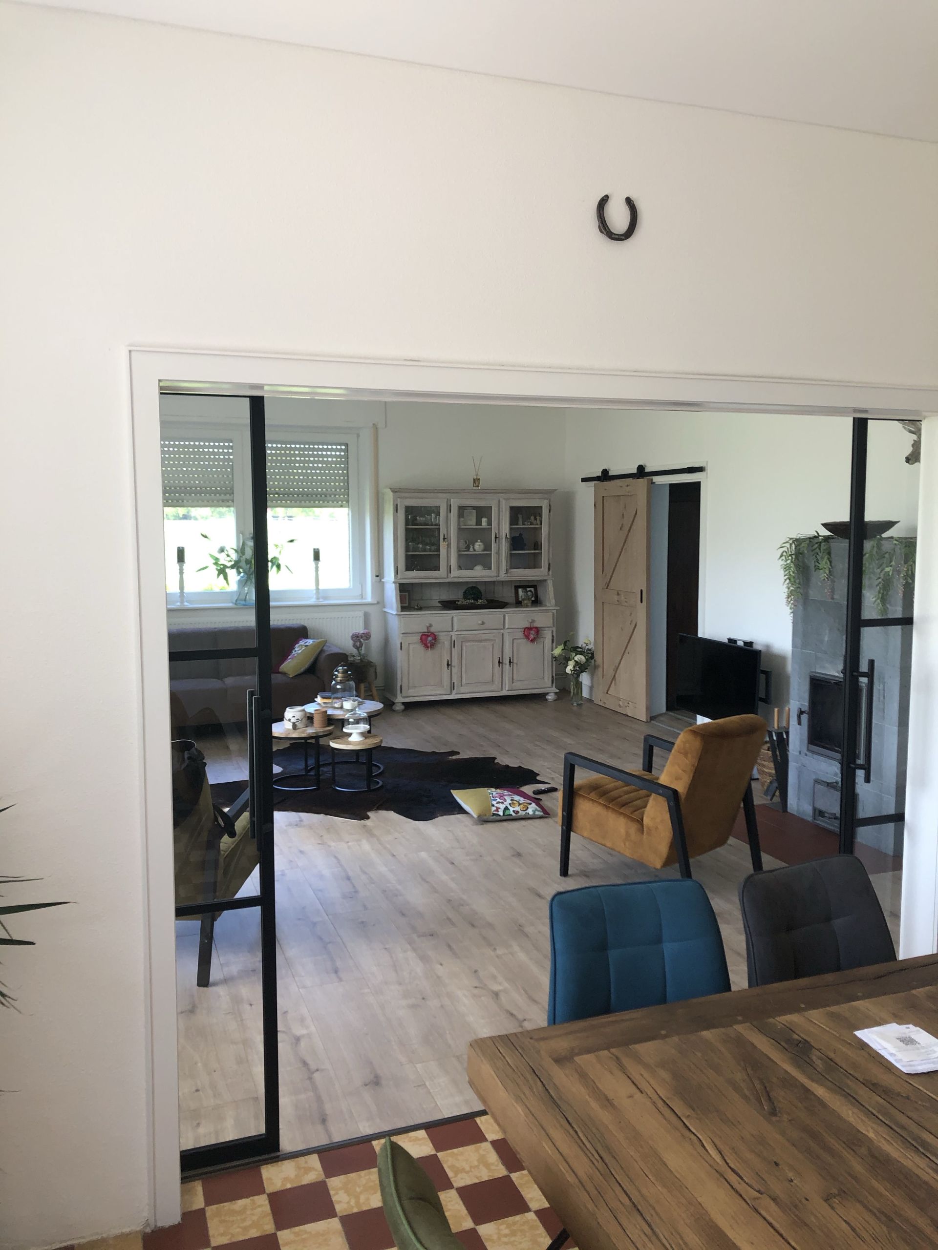 Blik op de woonkamer vanuit de eetkamer. Het gezellige interieur is zichtbaar, met meubilair en een decoratief hoefijzer.