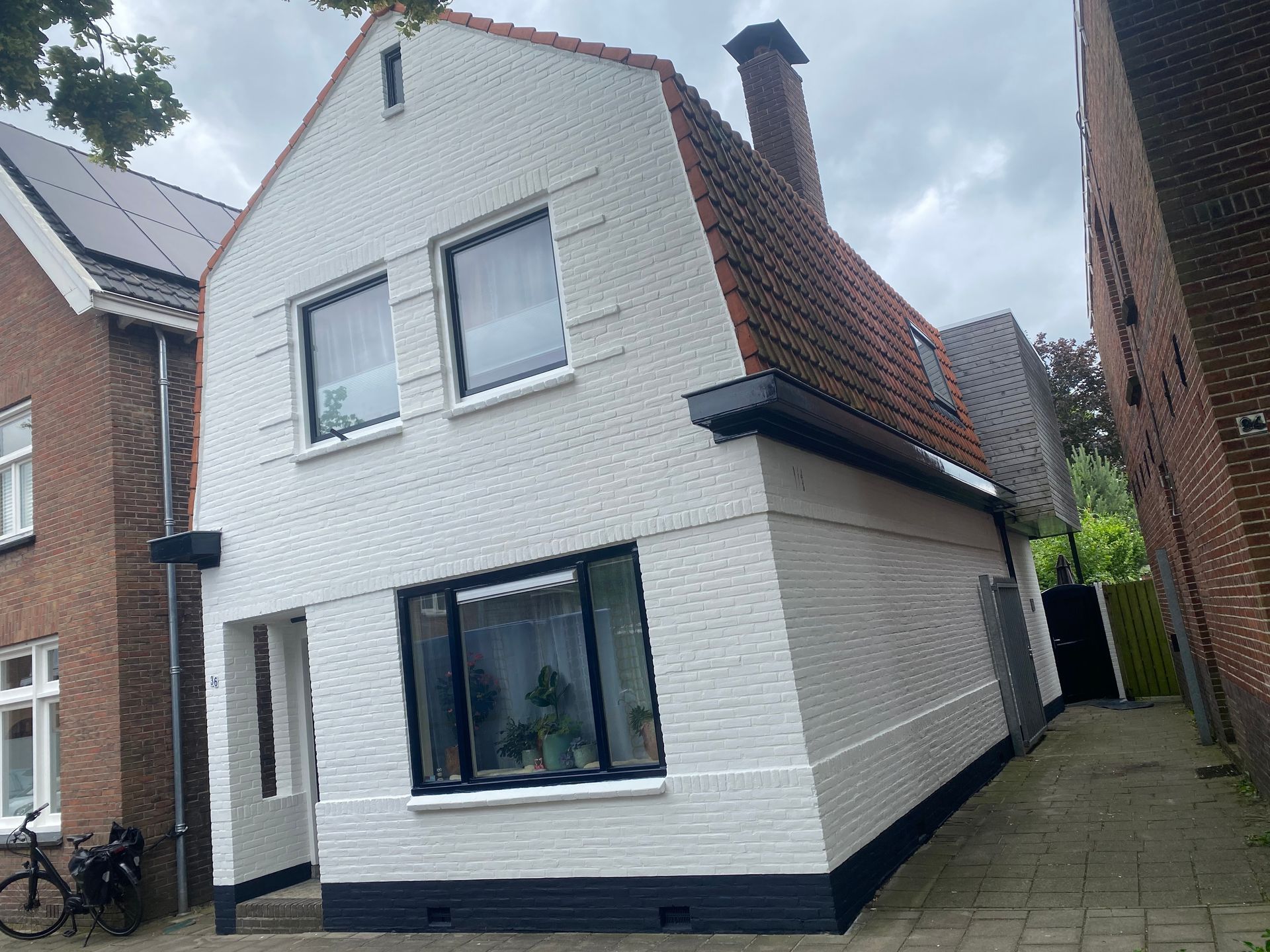 Wit bakstenen huis met zwarte accenten en een rood pannendak. 