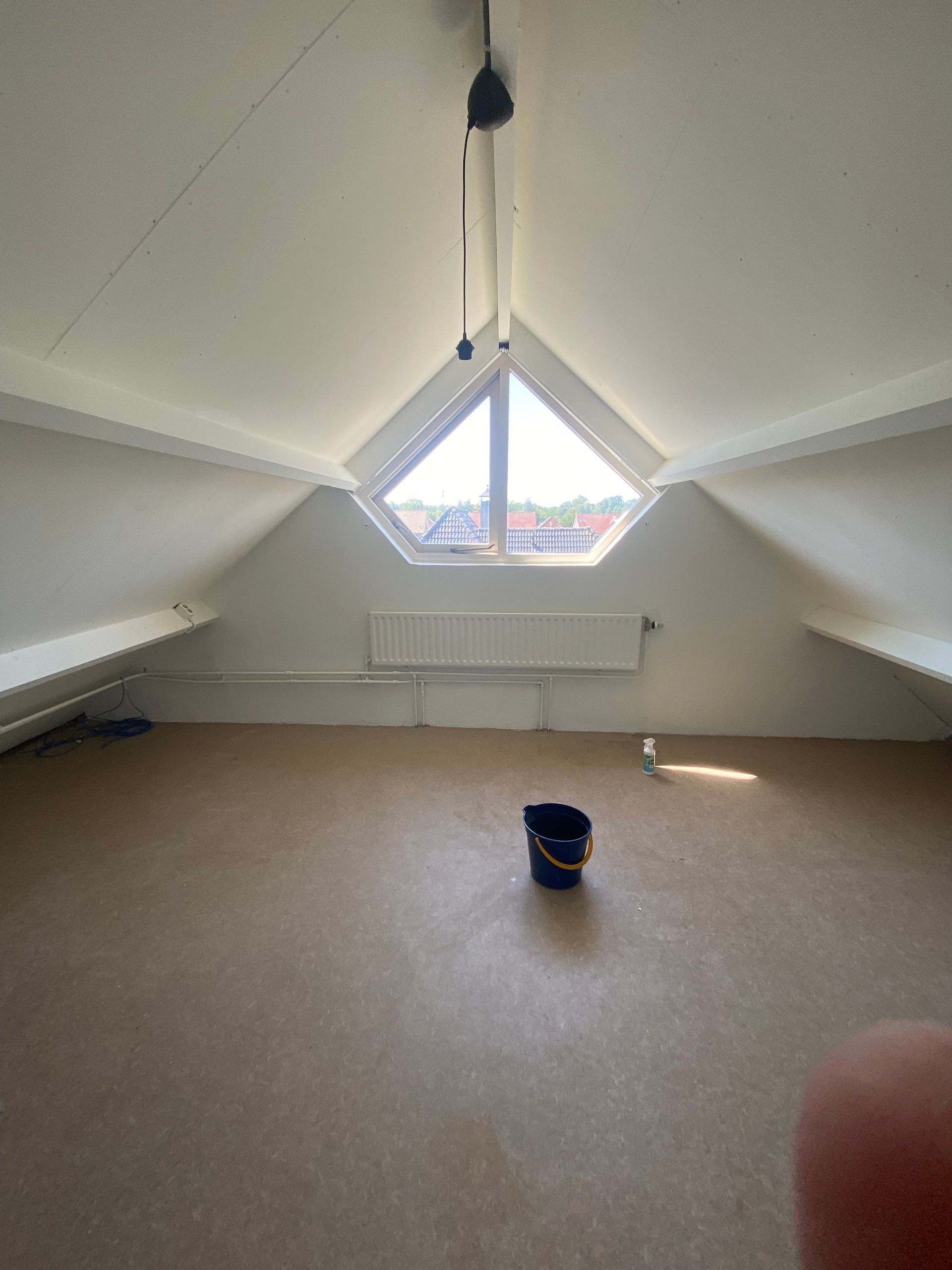Lege zolderkamer met een driehoekig raam, witte muren en plafond.