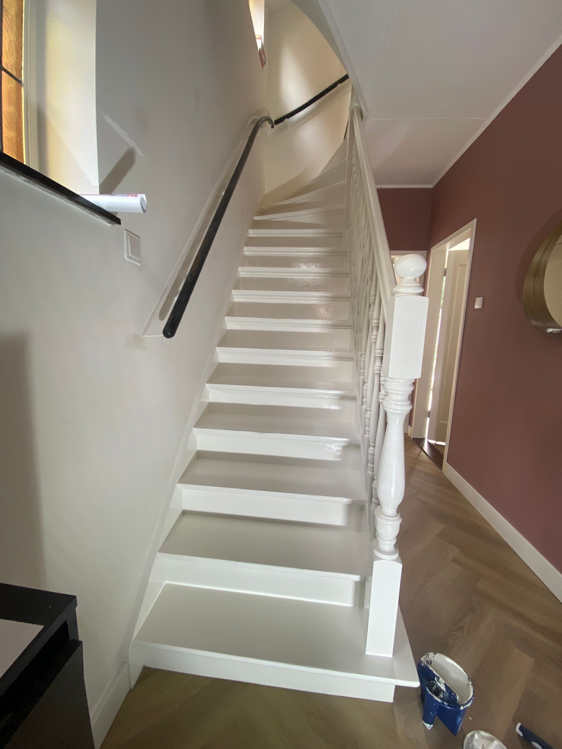Witte trap met zwarte leuning, omhoog lopend. Aangrenzend een gang met roze muur.