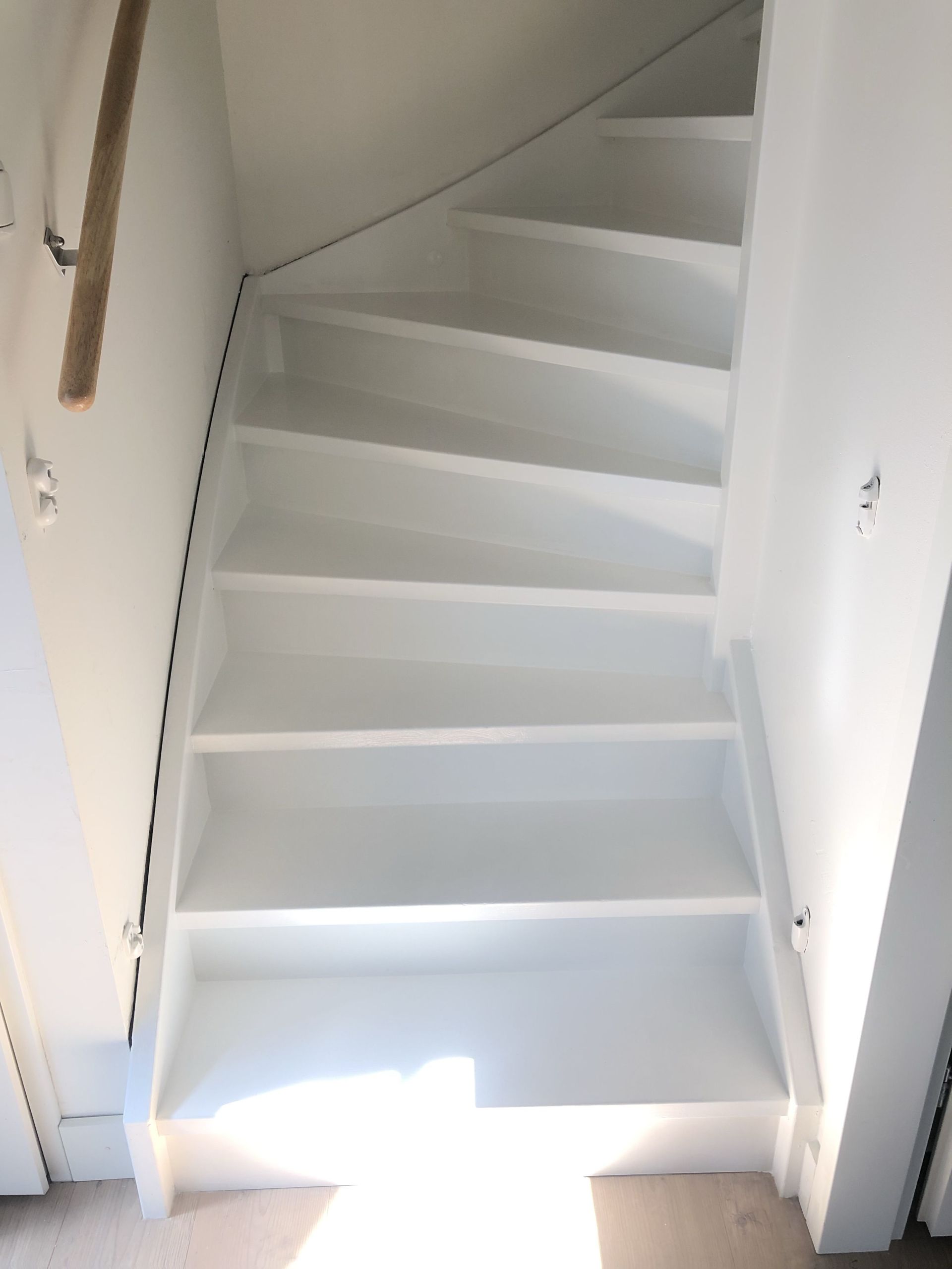 Witte houten trap die naar boven leidt, tussen witte muren.