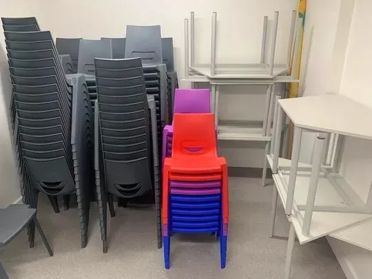 Store room with stacked gray, red, purple, and blue chairs, and tables.