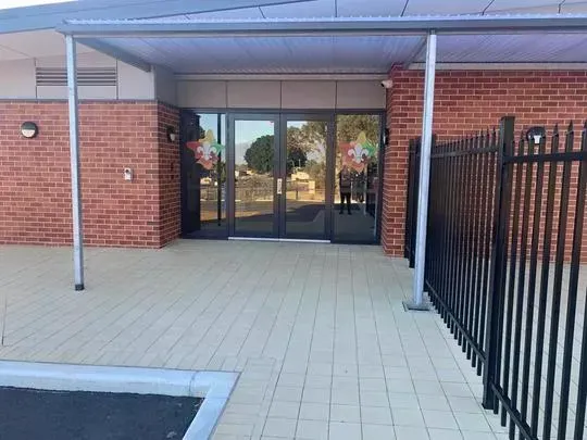 Entrance to a building with brick walls, glass doors, and a metal awning. Black fence to the right.