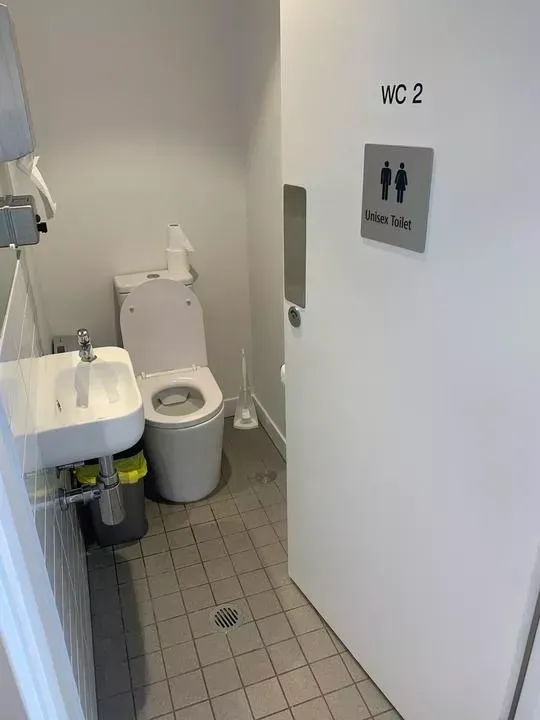 Unisex bathroom with a toilet, sink, and a dispenser.