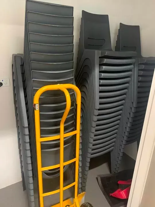 Stack of grey plastic chairs and a yellow hand truck instore room.