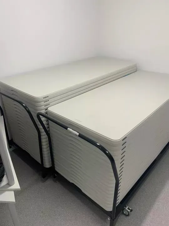 Two stacks of rectangular, beige tables on rolling carts, in a store room