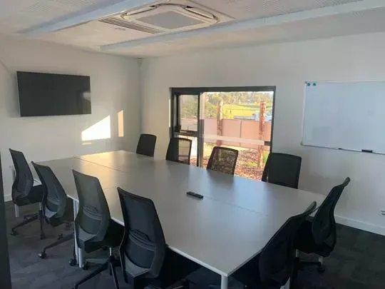 Conference room with large white table, black chairs, TV, whiteboard, and window.