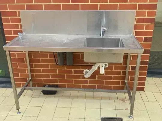 Stainless steel sink and table against a brick wall with filter water drinking tap.
