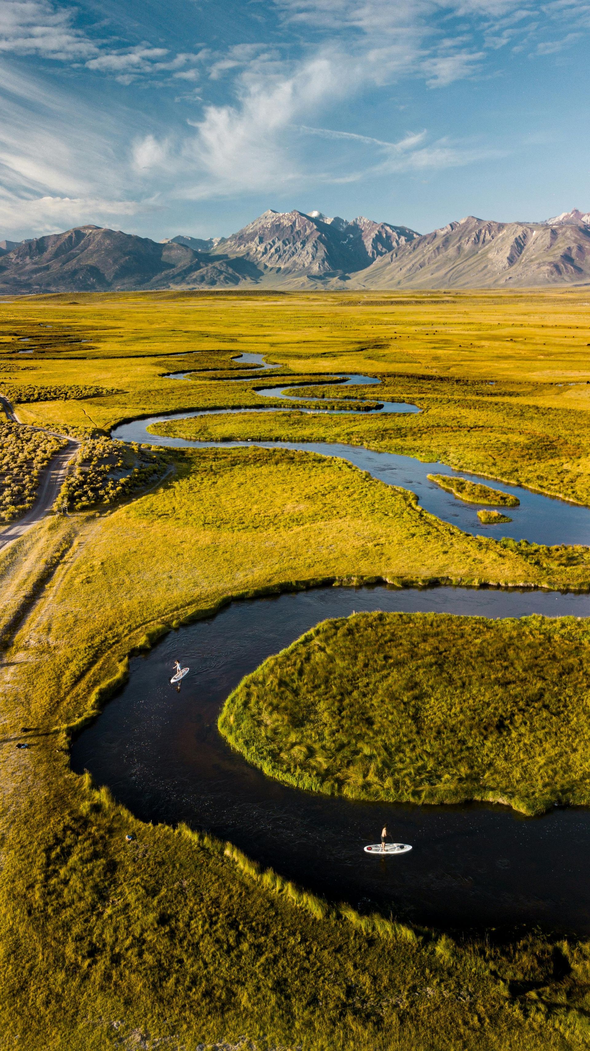 An aerial view of a river flowing through a lush green field with mountains in the background.