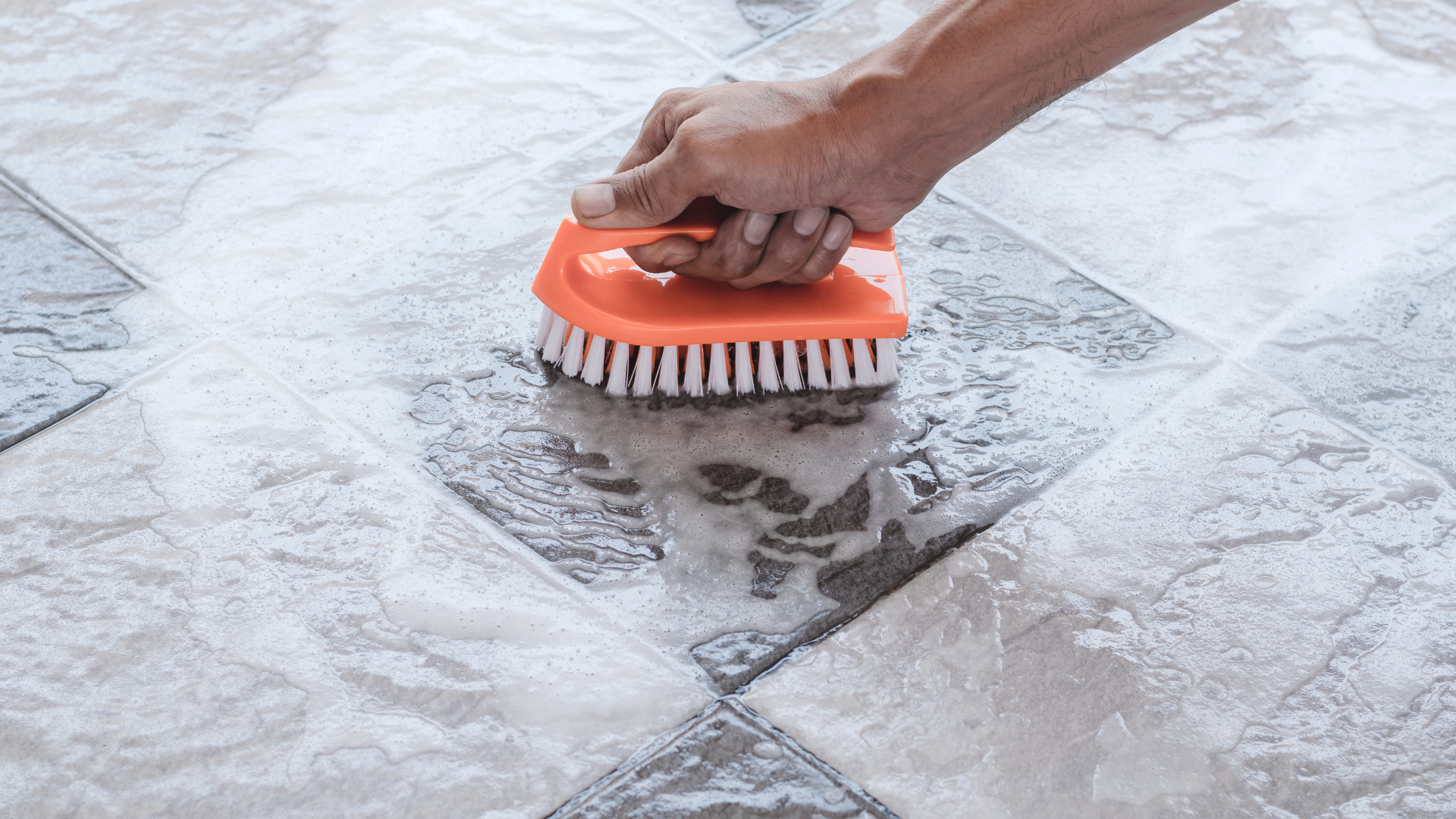 A person is cleaning a tile floor with a brush.