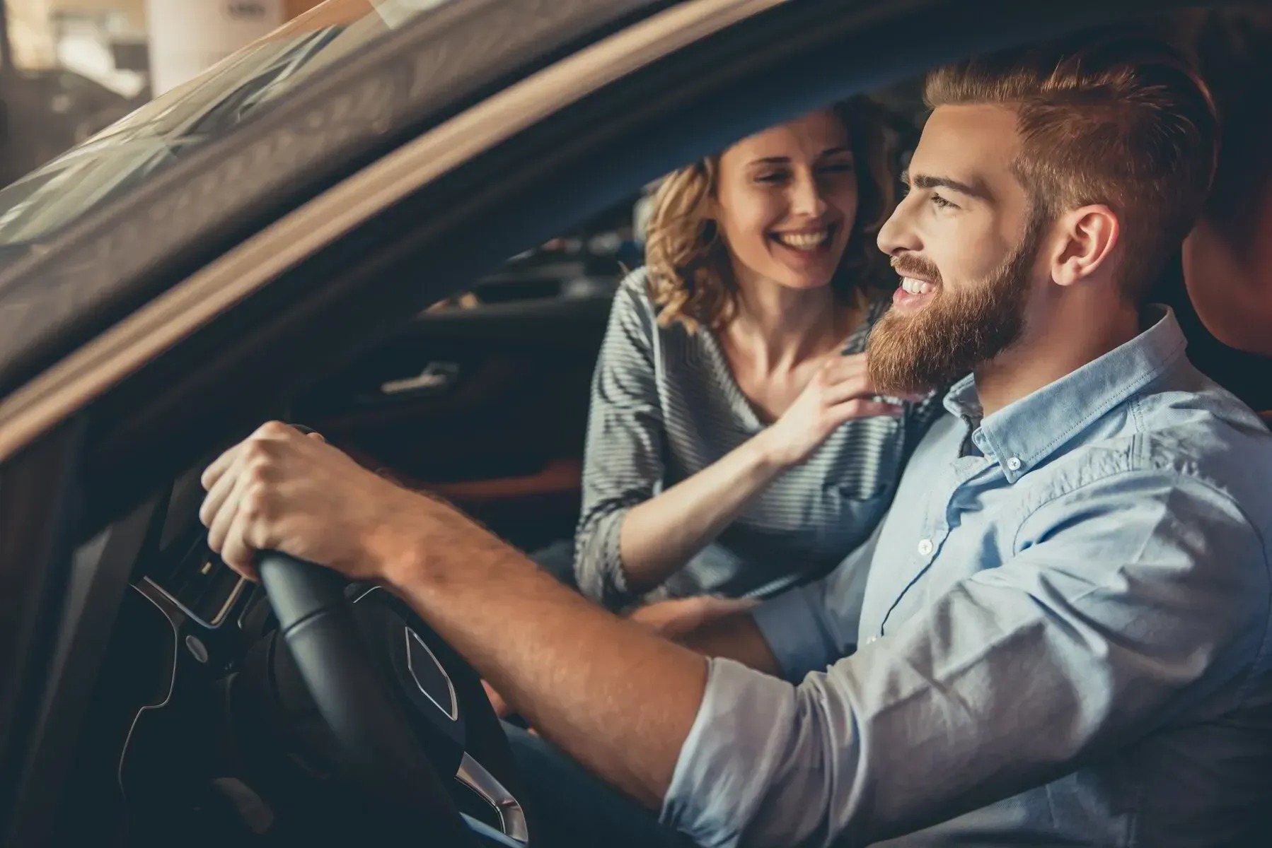 Man driving a car, smiling, with woman beside him touching his shoulder, interior shot.