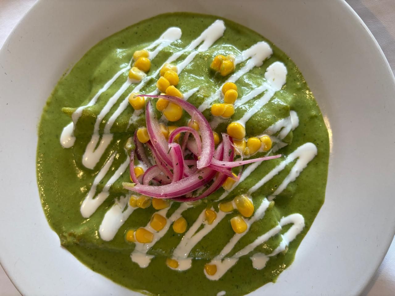 Enchiladas verdes cubiertas con maíz, cebollas encurtidas y salsa blanca.