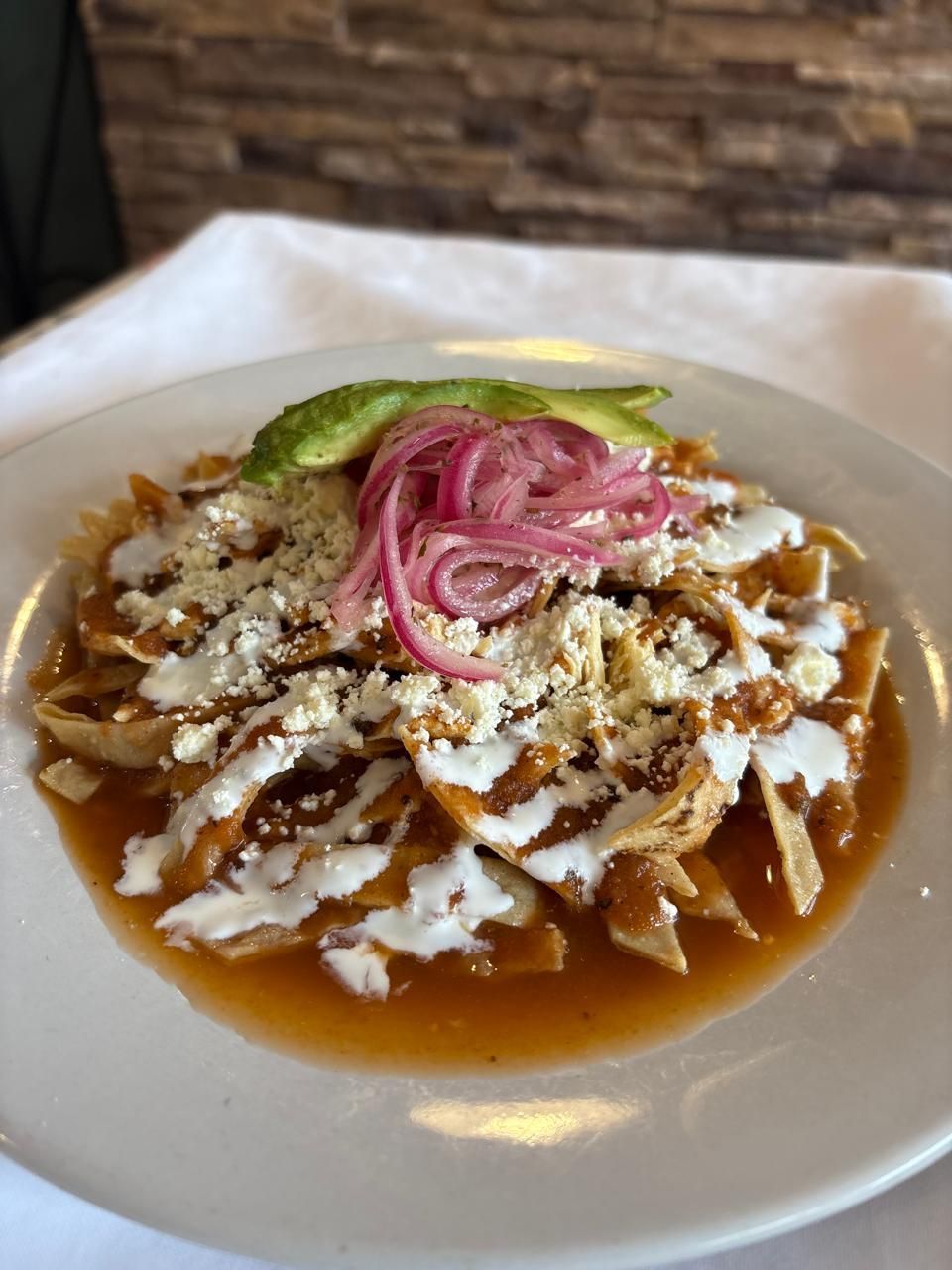 Chilaquiles en plato blanco, cubiertos con queso, cebolla y aguacate.