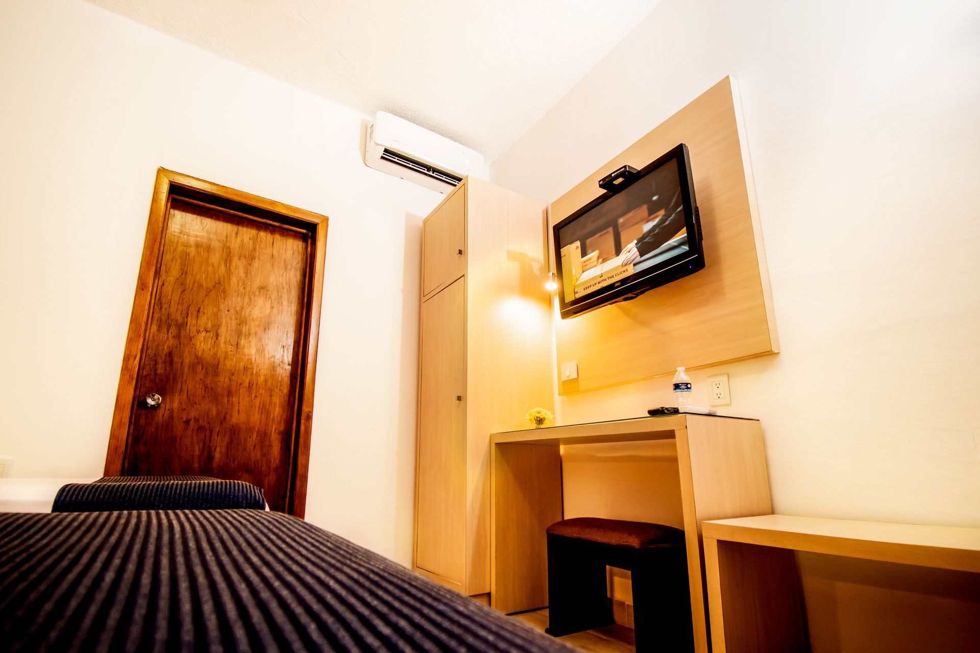 Habitación de hotel con cama, TV, escritorio, armario y puerta de madera.
