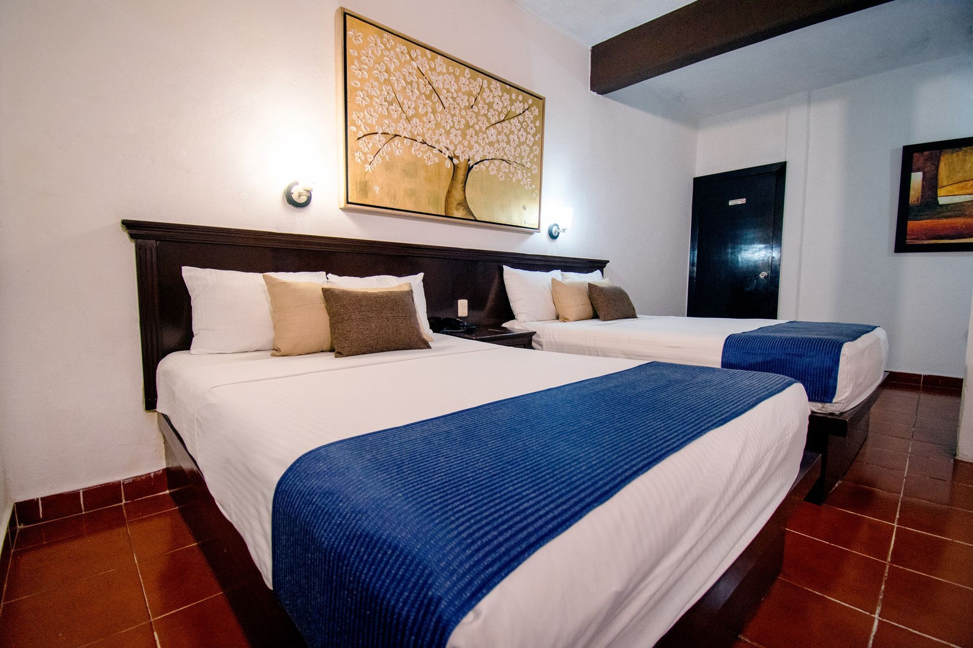 Habitación de hotel con dos camas queen, sábanas blancas, alfombras azules y arte en las paredes.