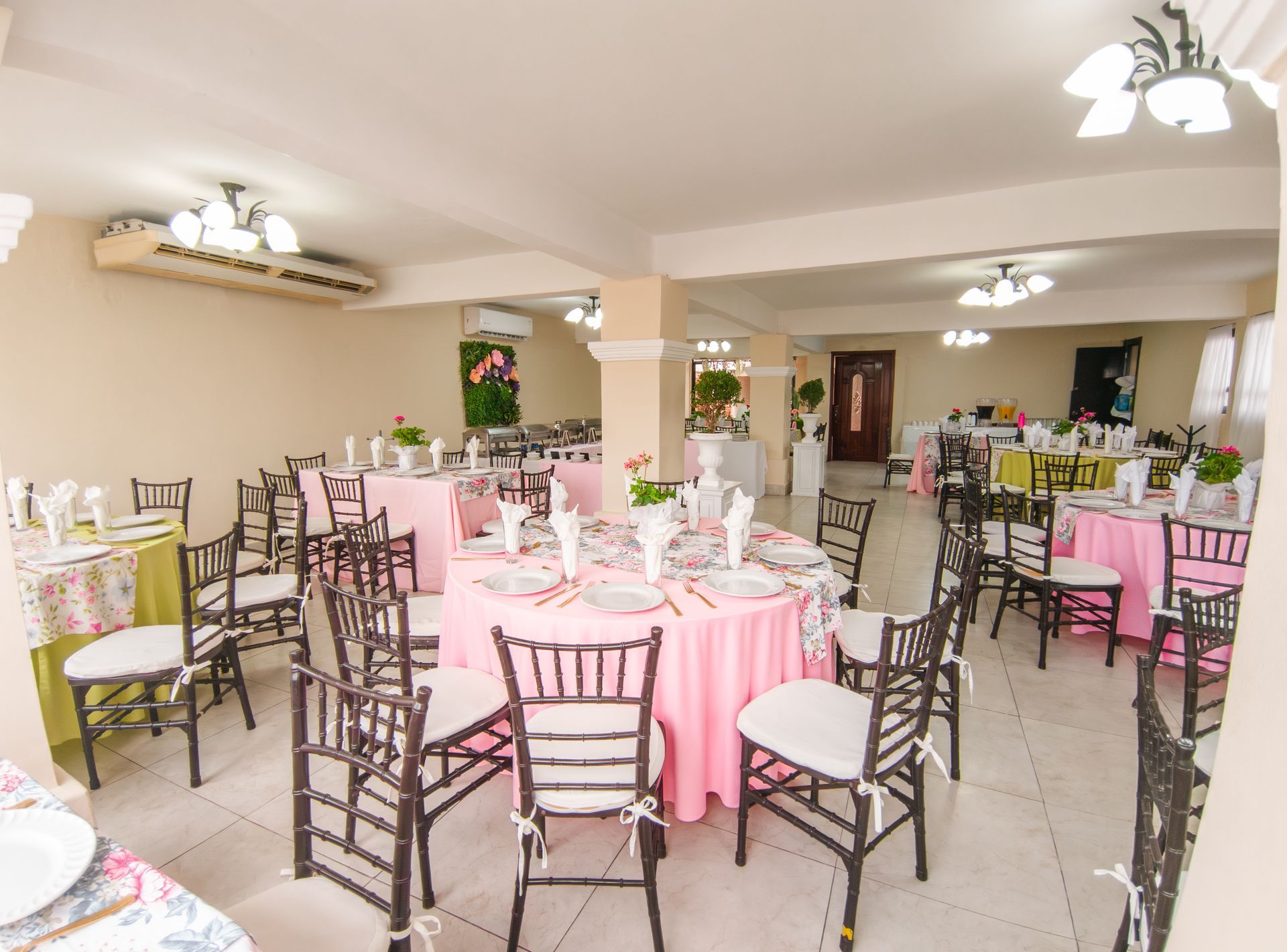 Interior de un salón de banquetes decorado con manteles, sillas y mesas de color rosa y verde listos para un evento.