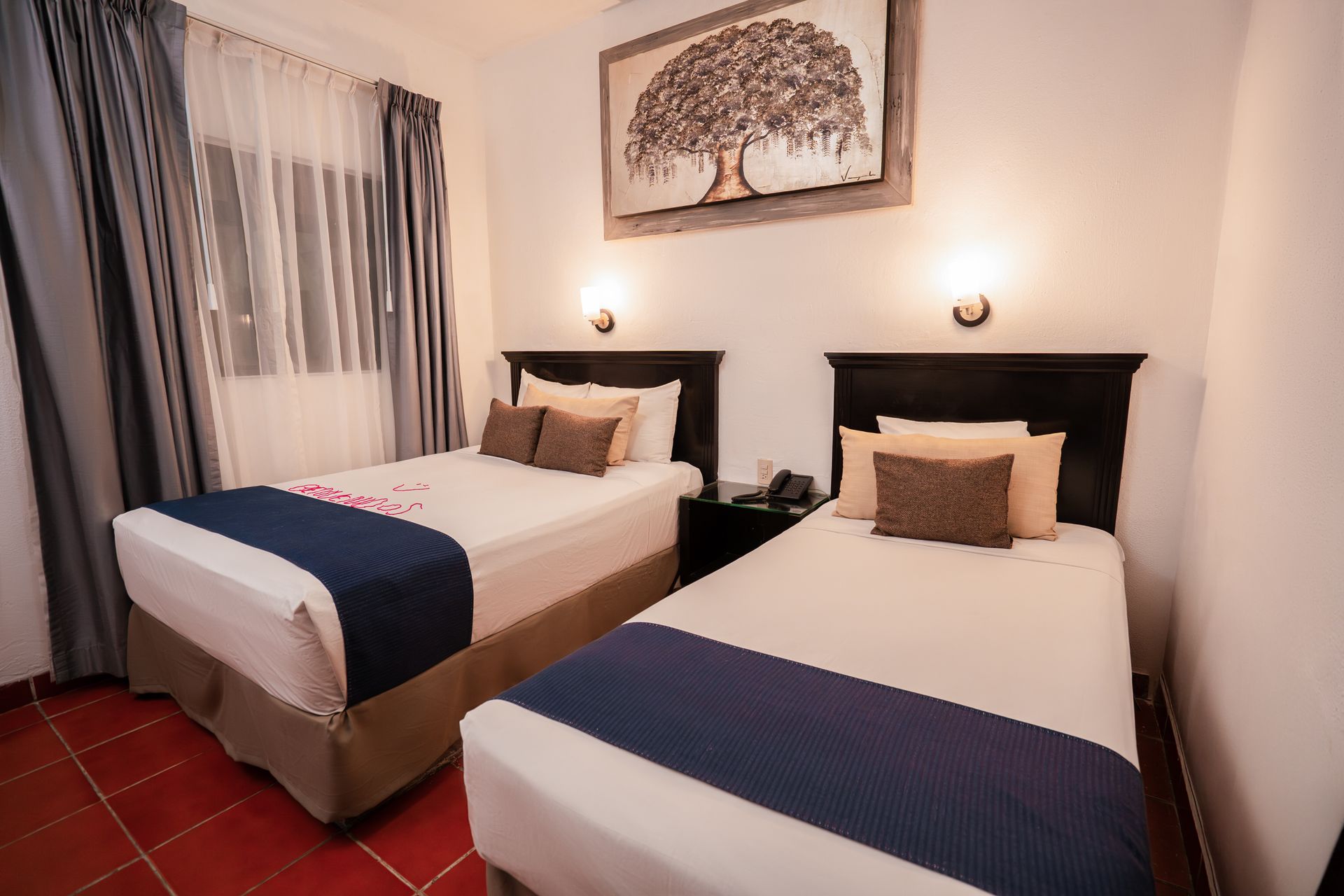 Dos camas individuales en una habitación de hotel con cabeceras oscuras, ropa de cama blanca, detalles en azul y arte encima.