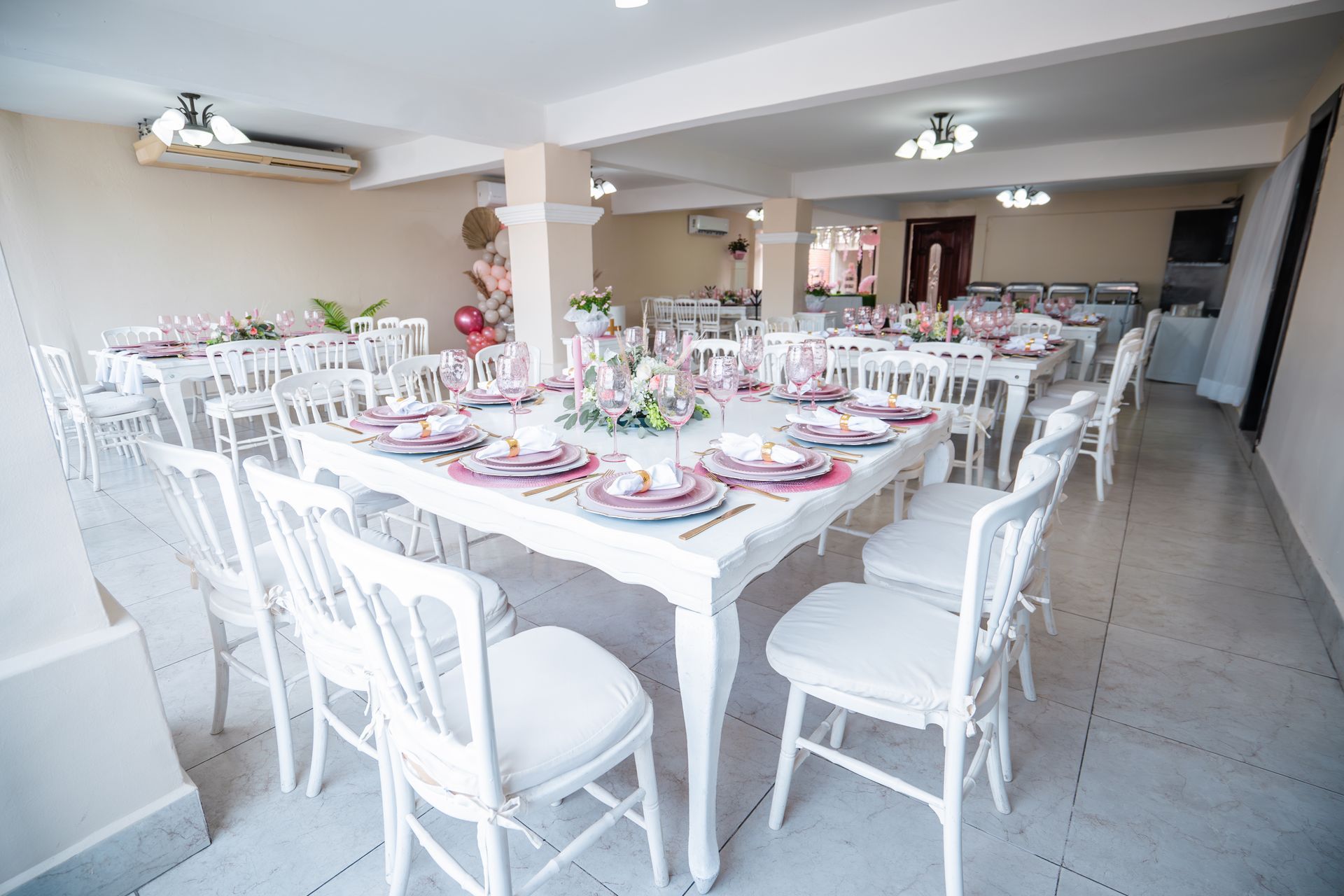 Mesas de comedor y sillas blancas colocadas para una fiesta en una habitación bien iluminada.