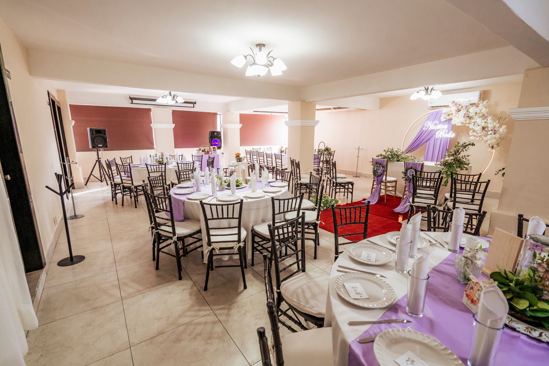 Salón de eventos formal con mesas redondas, sillas y decoraciones en color morado y blanco.