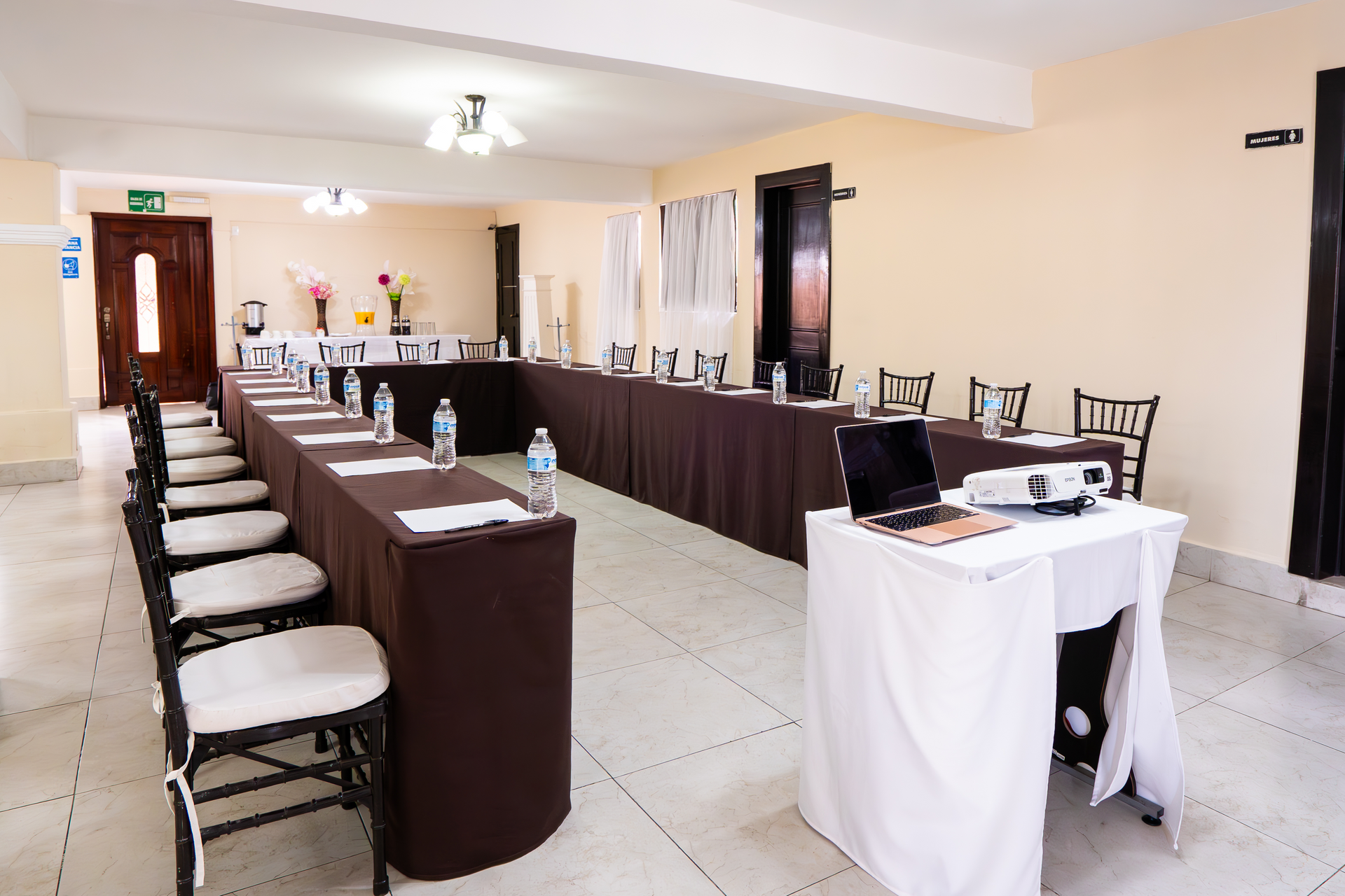 Sala de conferencias equipada con mesas, sillas, proyector y refrigerios.