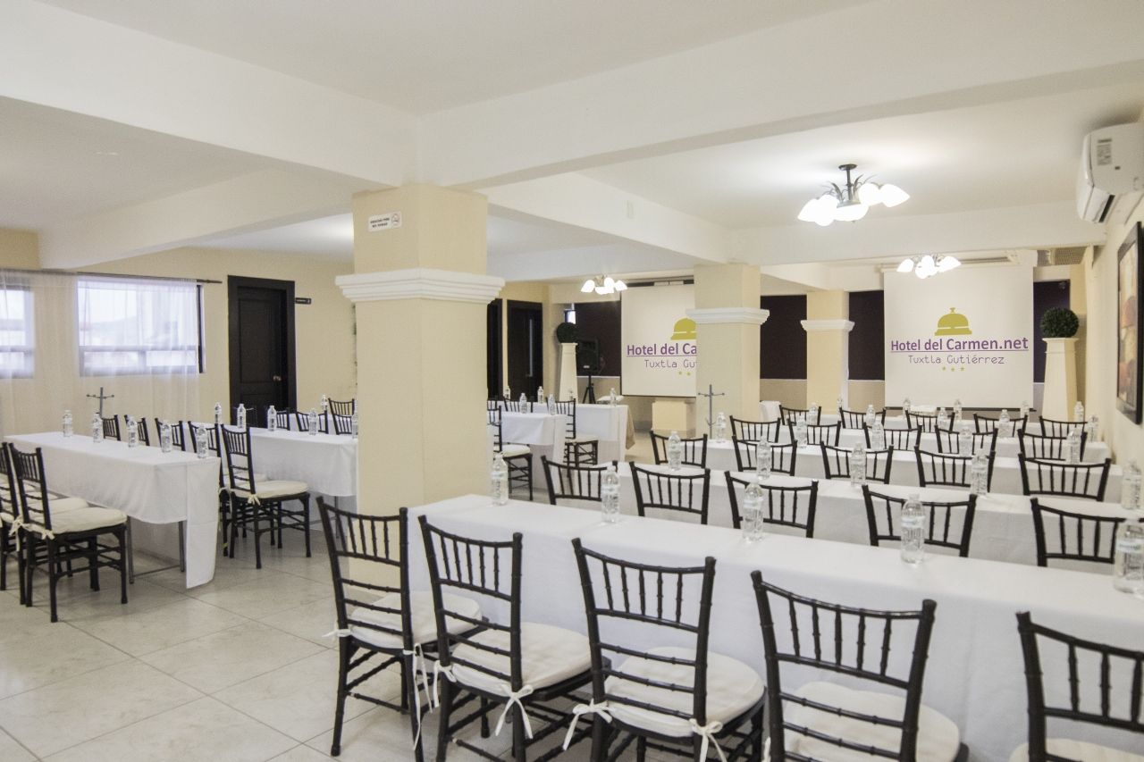 Salón de banquetes con mesas largas, mantelería blanca, sillas negras y pancartas promocionales.