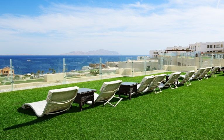 A row of lounge chairs on a green lawn overlooking the sea and a coastal resort under a clear blue sky.