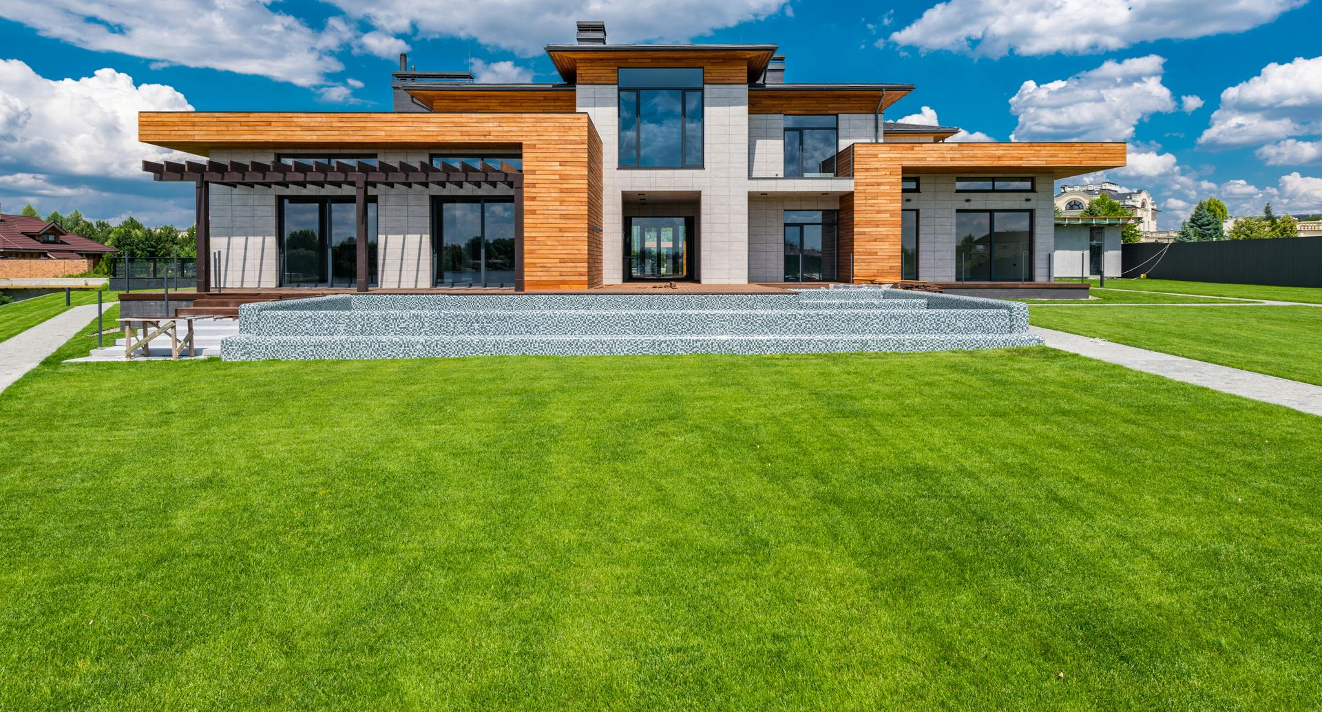 A modern two-story home with wood paneling and stone accents, featuring large glass windows, overlooking a green lawn.