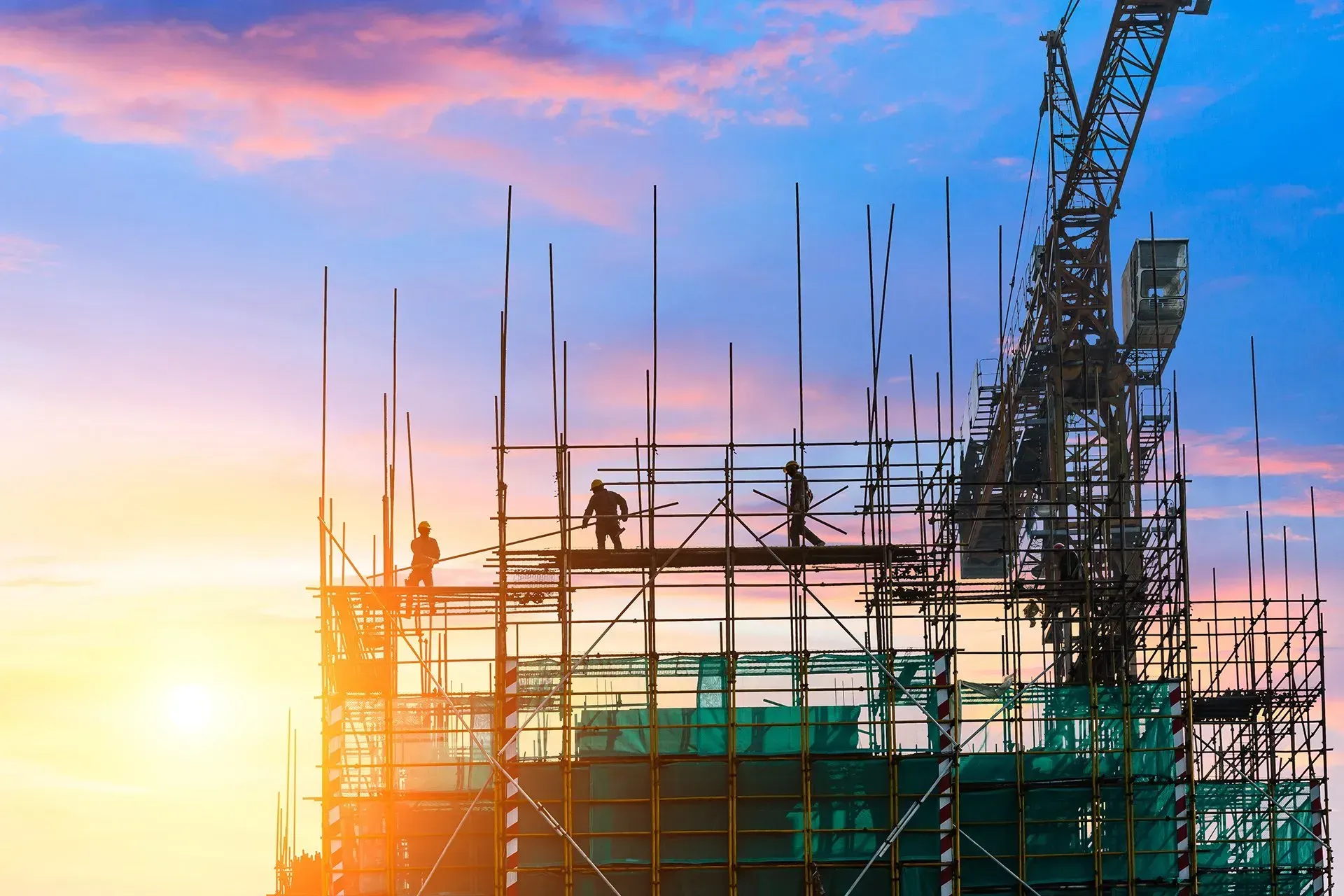 A construction site with scaffolding and a crane at sunset.