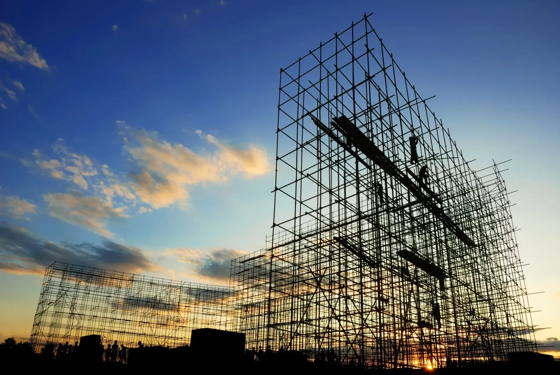 A large building is being built with scaffolding against a cloudy sky at sunset.