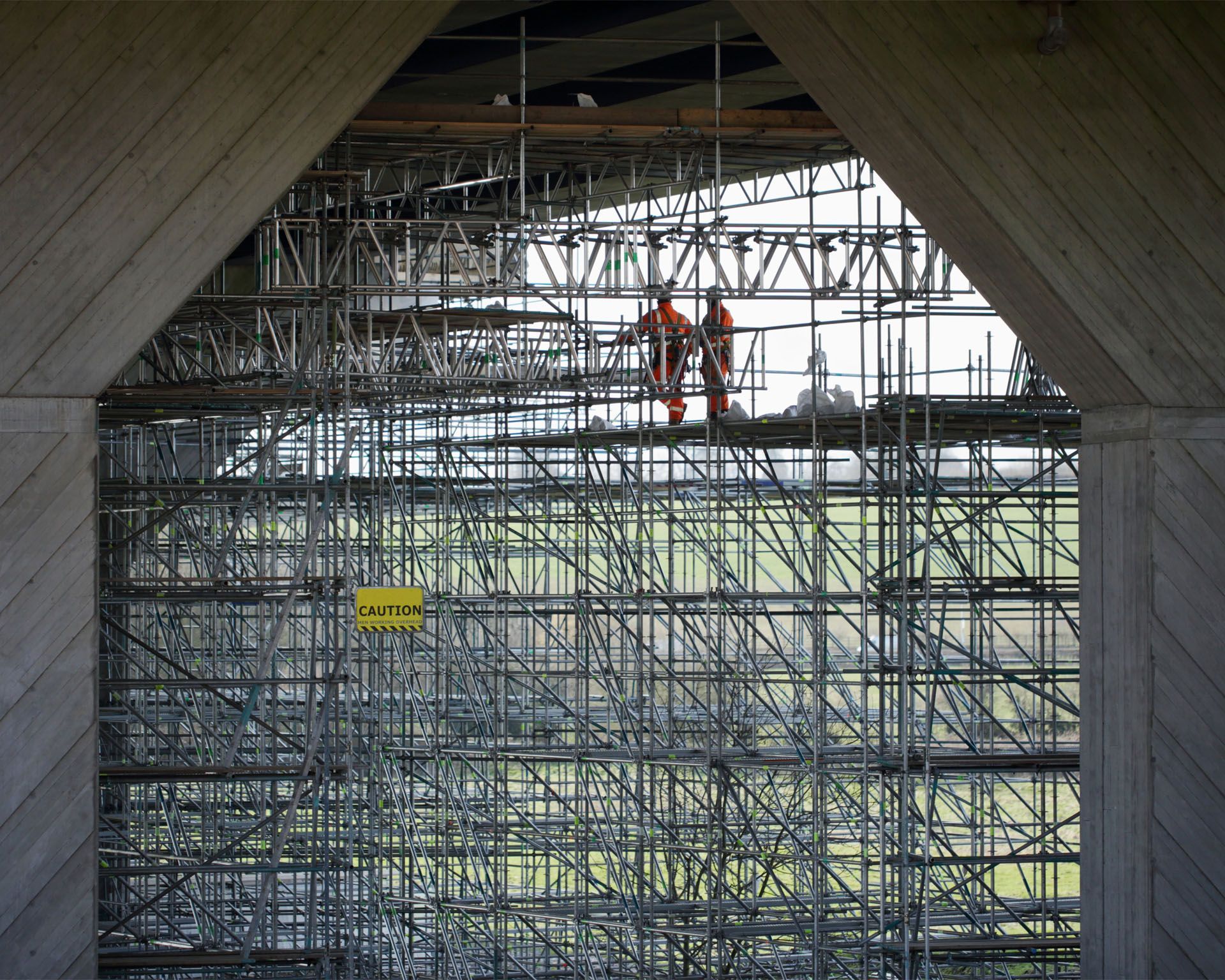 Two construction workers are standing on top of a scaffolding structure