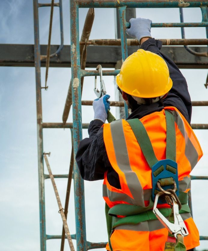 Construction worker in safety gear climbing on metal structure.