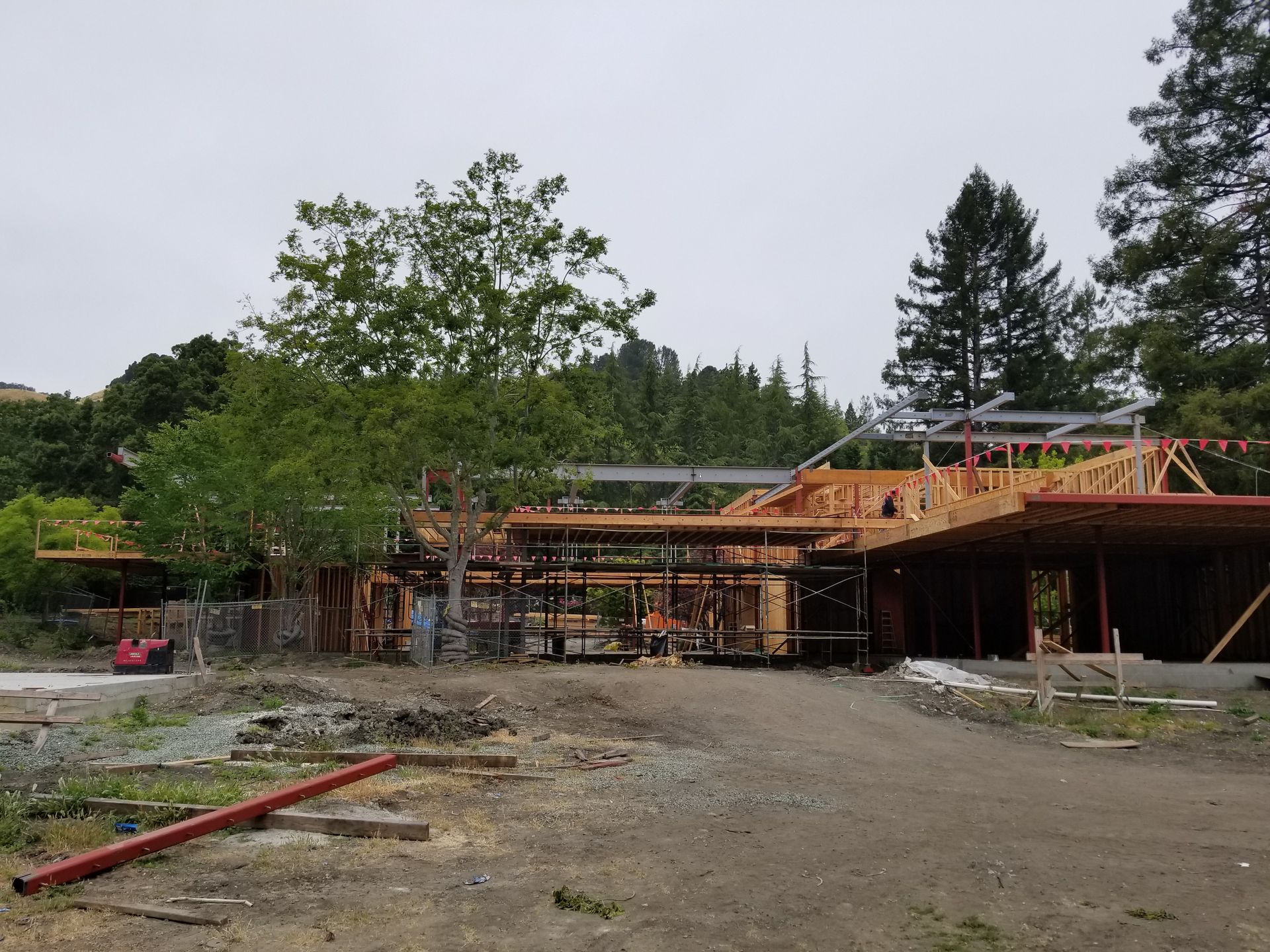 A large house is being built in the middle of a dirt field surrounded by trees.