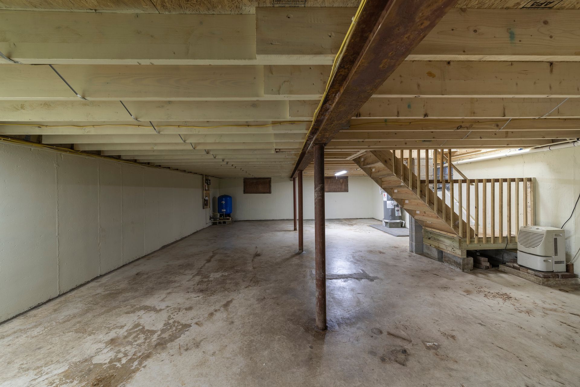 An empty basement with a wooden staircase leading up to the second floor.